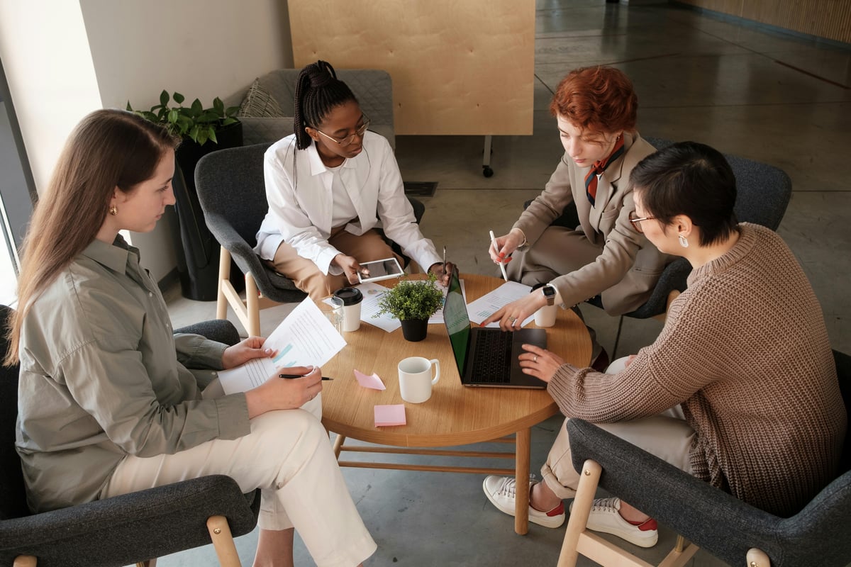 Four colleagues reviewing printed documents and a laptop around a low table