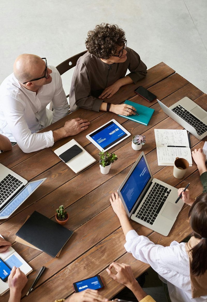 Overhead view of a team reviewing documents on laptops and tablets around a wooden table