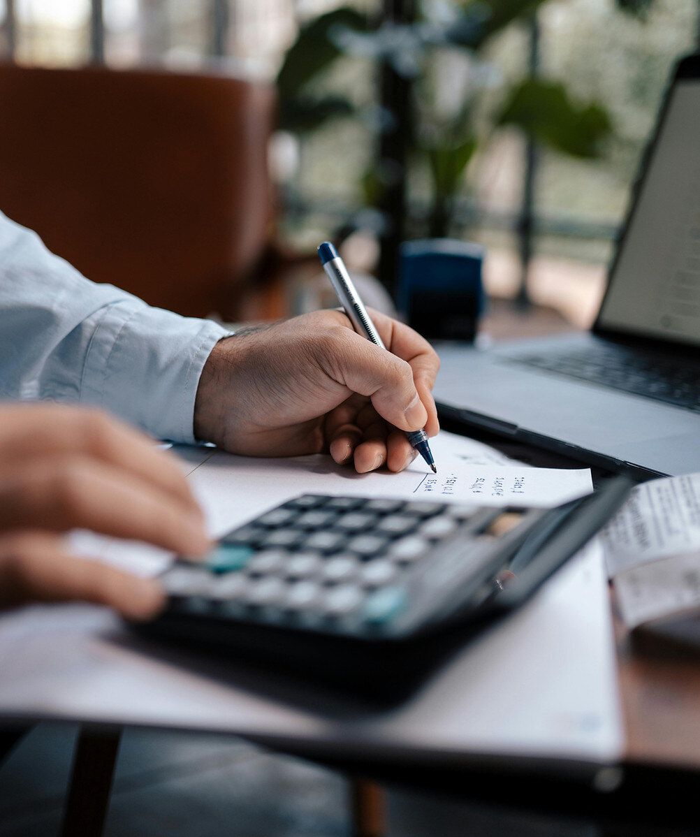 Close-up of a person working through figures on a calculator beside handwritten notes